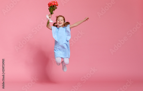 funny child girl runs and jumps with bouquet of flowers on colored background