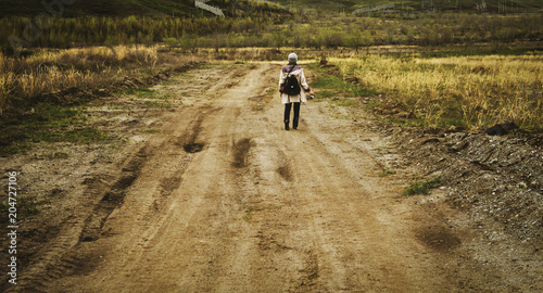 A woman is walking on a country road through yellow fields. Female photographer. Vintage effects. Walking in the nature. Country road. Countryside