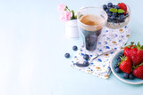 A glass of coffee and pudding chia with blueberries and strawberries for breakfast. Vegetarian food. A small bouquet of flowers and a blue background.
