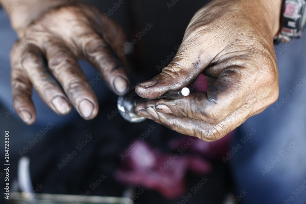 dirty, greasy Asian man's hands, oiling and greasing valves and pistons and inserting into an engine block in a dirty workshop in Thailand, Southeast Asia