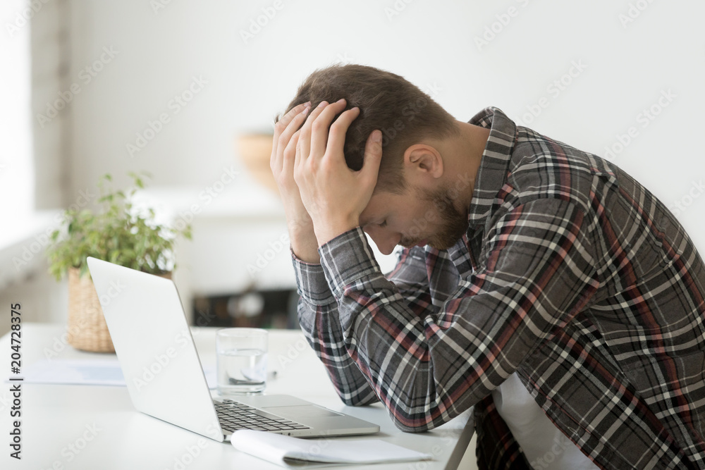 Frustrated depressed man holding head in hands shocked by bankruptcy stock downfall sitting at work desk with laptop, stressed tired businessman feels despair lost money online or got problem debt Frustrated depressed man holding head in hands shocked by bankruptcy stock downfall sitting at work desk with laptop, stressed tired businessman feels despair lost money online or got problem debt