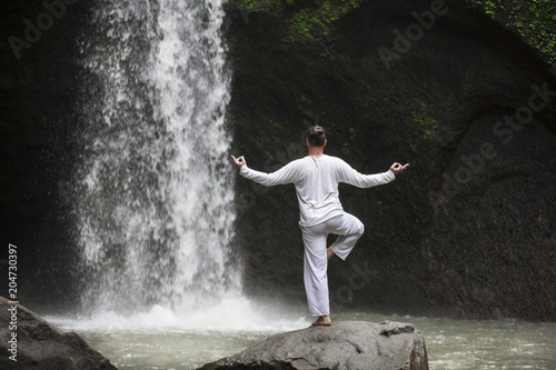 Man standing in meditation yoga on rock at waterfall