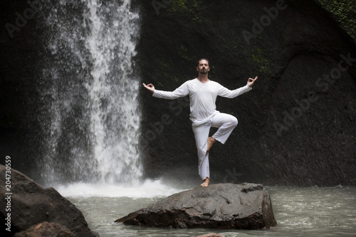 Man standing in meditation yoga on rock at waterfall