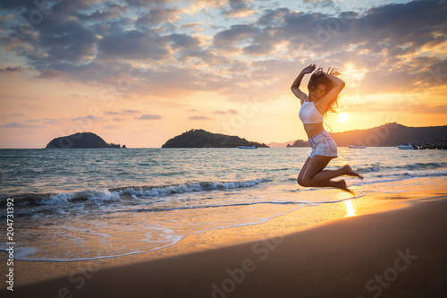 Travel woman jumping on beach in sunset