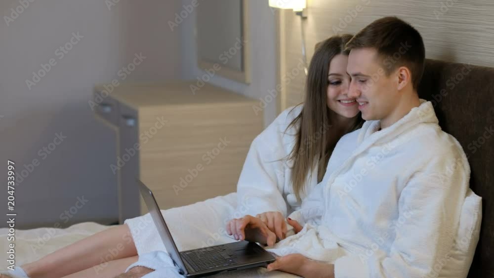 social network addiction. idle leisure and communication. couple using laptop at home before going to sleep. man and woman lie in bed in bathrobes social network addiction. idle leisure and communication. couple using laptop at home before going to sleep. man and woman lie in bed in bathrobes