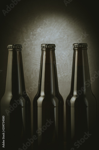 three black bottles of beer on a dark background with light/three black bottles of beer on a dark background with light. Selective focus
