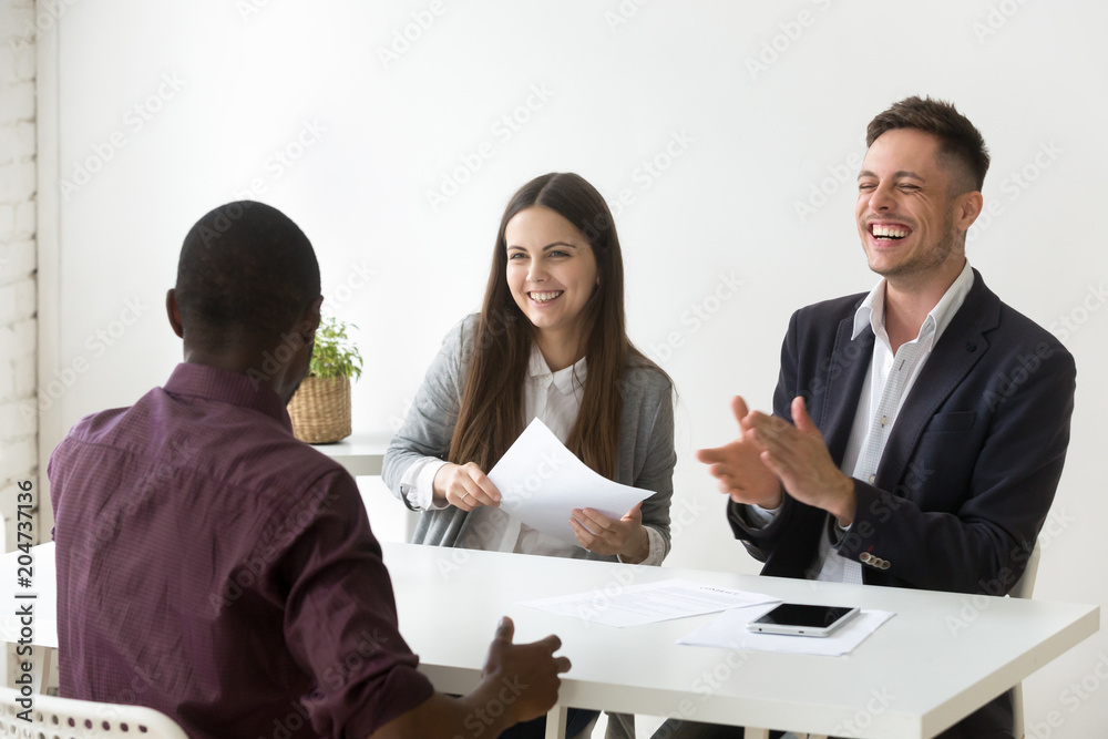 African american applicant make caucasian hr laugh at successful job interview, black candidate telling funny joke while talking to happy smiling recruiters, good first impression and hiring concept African american applicant make caucasian hr laugh at successful job interview, black candidate telling funny joke while talking to happy smiling recruiters, good first impression and hiring concept