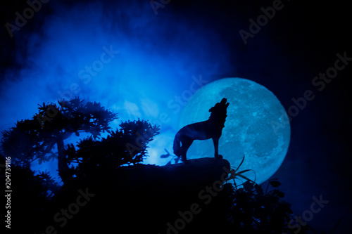 Obraz na płótnie Silhouette of howling wolf against dark toned foggy background and full moon or Wolf in silhouette howling to the full moon