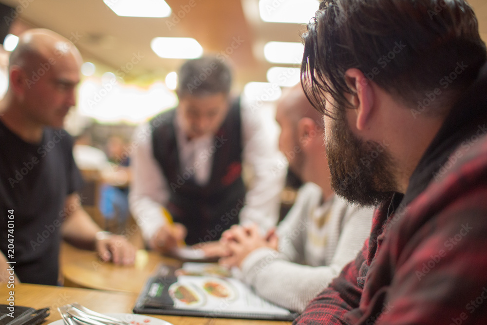 Group of men sitting in a restaurant ready to order. Selective focus