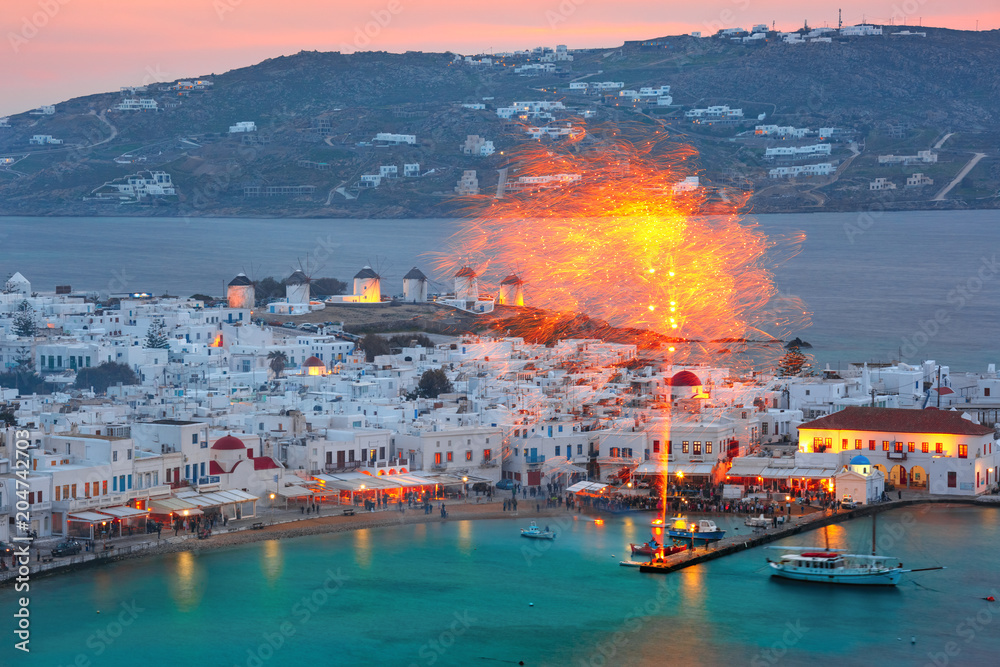 Aerial view of Mykonos City, Chora with Old Port, white houses, windmilles and churches on the island Mykonos, The island of the winds, during evening blue hour, Greece