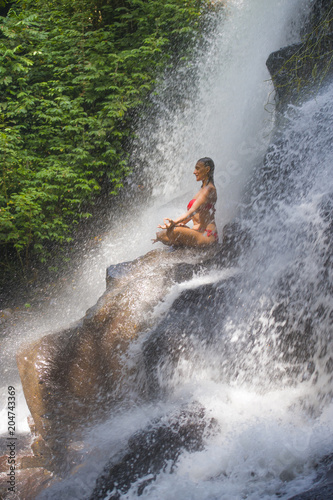 young attractive and happy 30s woman with fit body practicing yoga wet under tropical paradise waterfall stream in meditation and relaxation