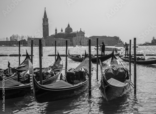 Sicht von Venedig, schwarzweiss Aufnahme von angebundene Venezianische Gondeln im hellen Tageslicht, im Hintergrund Gondoliere und Lagune sowie San Giorgio Maggiore © Thomas