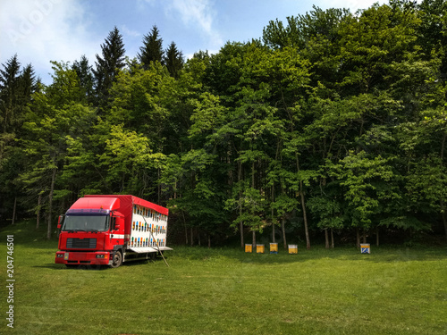 A bee hive truck on a fresh green meadow with trees in the background on a sunny day.