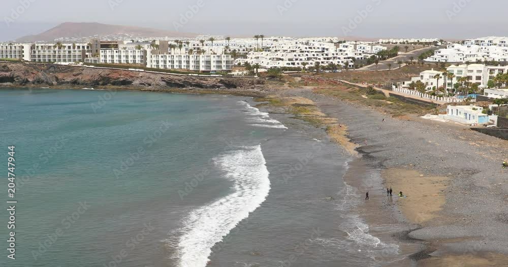 Ocean waves in the south of Lanzarote Island with white houses of Playa Blanca on the background, Canary Islands, Spain Ocean waves in the south of Lanzarote Island with white houses of Playa Blanca on the background, Canary Islands, Spain