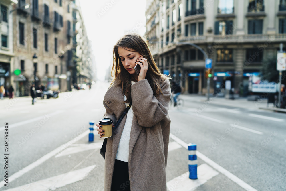 Successful business woman making business calls by a mobile phone to the partners while going to office with coffee. Fashionable hipster girl wearing stylish clothes chatting with friend by smartphone