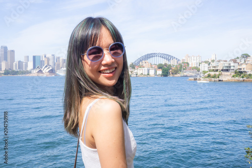 Young woman stands on the background of the beautiful Sydney skyline on a sunny day in a white dress and sunglasses © kimlongcreations
