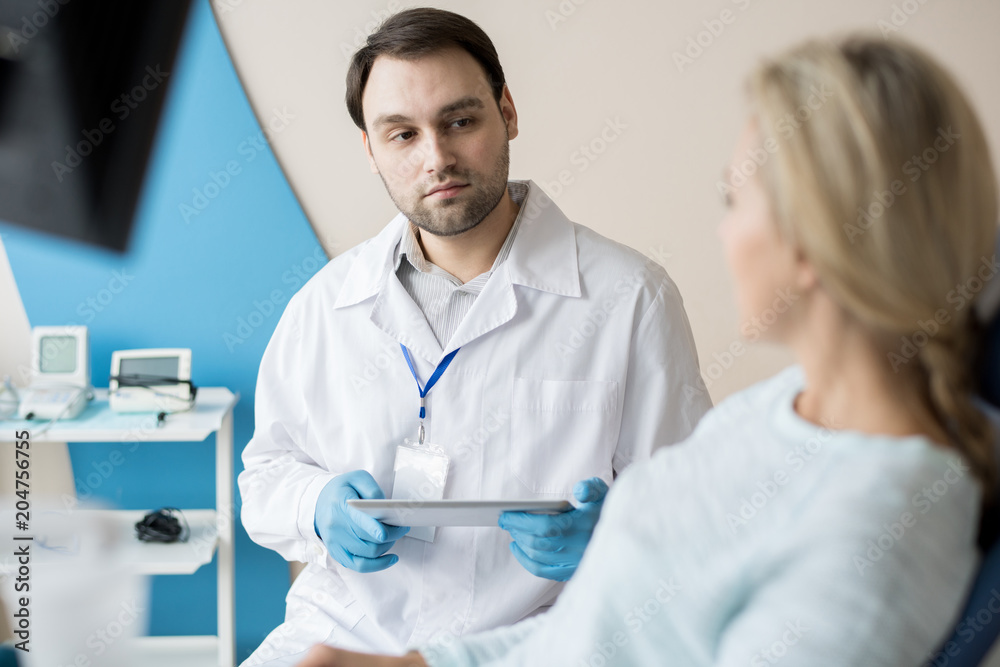 Confident man in white gown and gloves having talk to woman working in dentistry cabinet. Confident man in white gown and gloves having talk to woman working in dentistry cabinet.