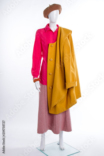 Female mannequin with yellow coat. Beret, blouse, skirt and overcoat. Women fashion look.