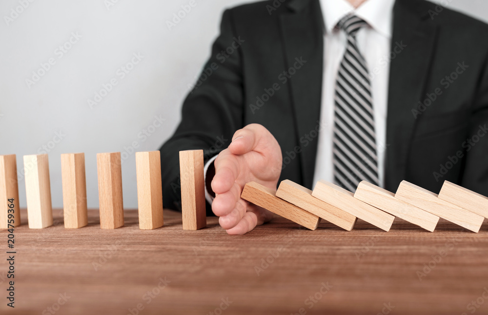 Businessman stopping domino effect with his hand. Security and insurance concept