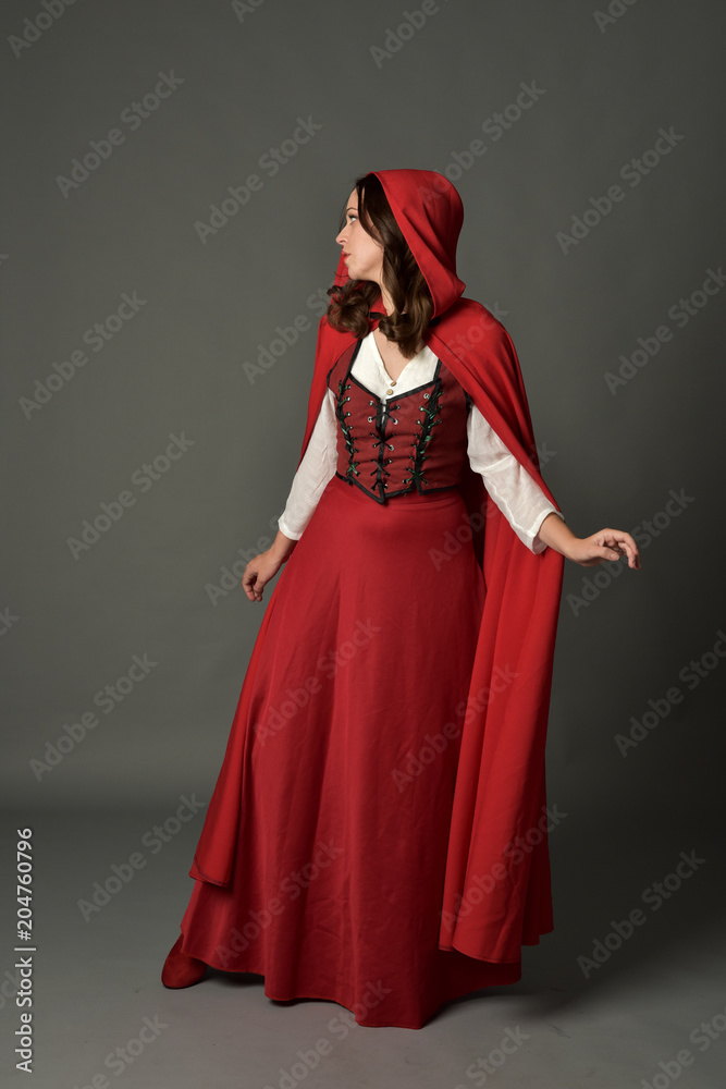 full length portrait of woman wearing red fantasy costume with cloak, standing pose on grey studio background. full length portrait of woman wearing red fantasy costume with cloak, standing pose on grey studio background.