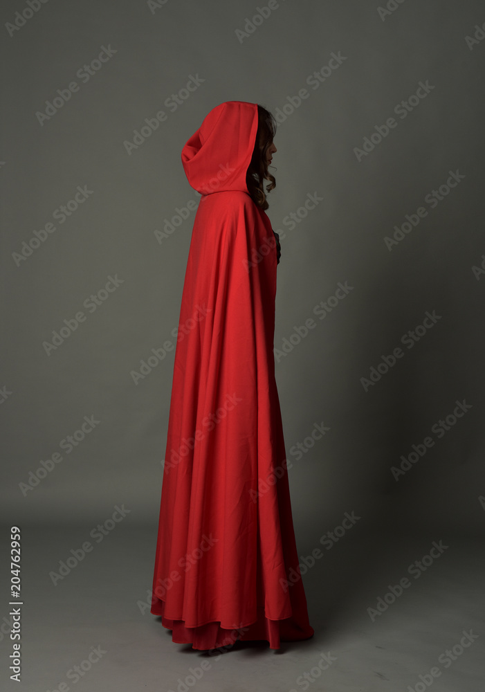 full length portrait of woman wearing red fantasy costume with cloak, standing pose on grey studio background. full length portrait of woman wearing red fantasy costume with cloak, standing pose on grey studio background.