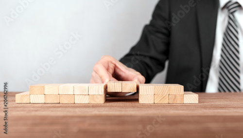 Close up of hand of businessman assembling a bridge made from little blocks.