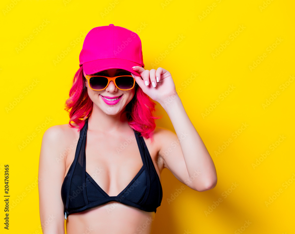 Young pink hair girl in bikini and orange glasses with cap. Portrait isolated on yellow background Young pink hair girl in bikini and orange glasses with cap. Portrait isolated on yellow background