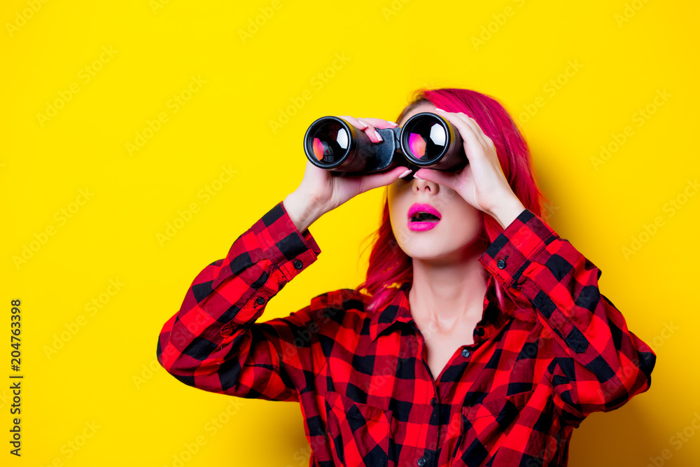 Young redhead girl with binoculars. Portrait isolated on yellow background Young redhead girl with binoculars. Portrait isolated on yellow background
