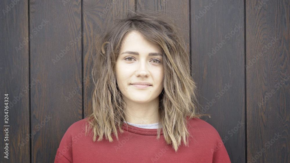 Fototapeta premium A young cute casual brunette girl in a red sweatshirt on a wooden brown background