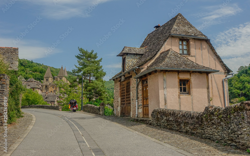Conques, Midi Pyrenees, France - July 31, 2017: Typical house at the entrance to the village of Conques with the Cathedral of Sainte Foy at the back Conques, Midi Pyrenees, France - July 31, 2017: Typical house at the entrance to the village of Conques with the Cathedral of Sainte Foy at the back