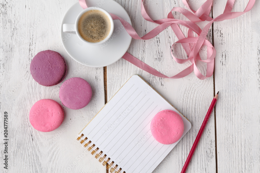 Coffee, cake macaron, clean notebook, eyeglasses and flower on pink table from above. Female working desk. Cozy breakfast. Flat lay style. Coffee, cake macaron, clean notebook, eyeglasses and flower on pink table from above. Female working desk. Cozy breakfast. Flat lay style.