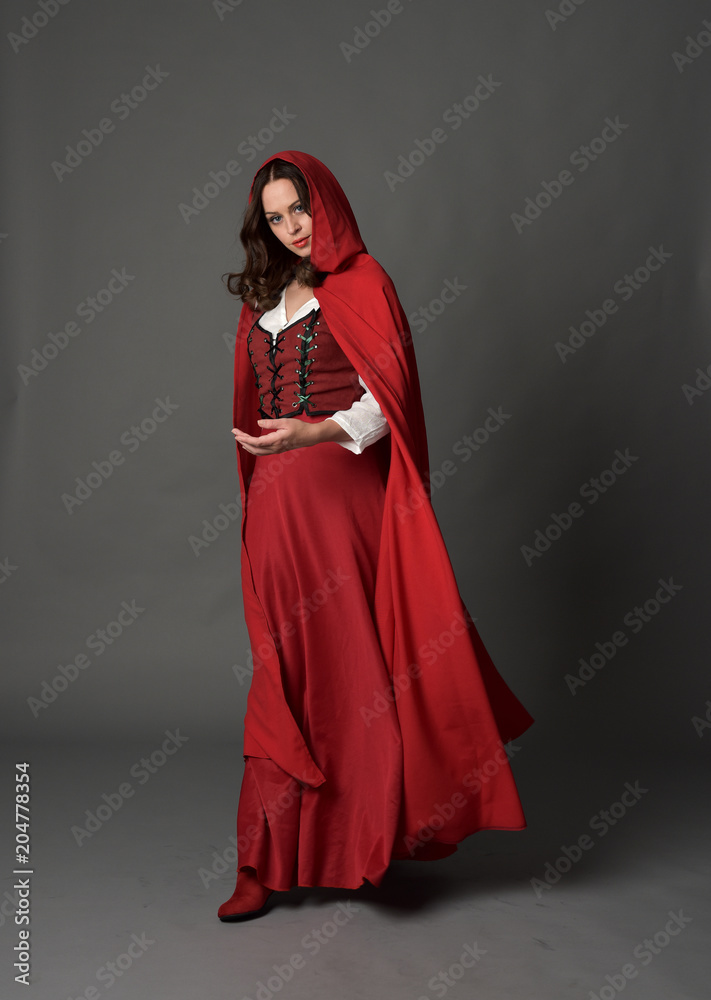 full length portrait of woman wearing red fantasy costume with cloak, standing pose on grey studio background. full length portrait of woman wearing red fantasy costume with cloak, standing pose on grey studio background.
