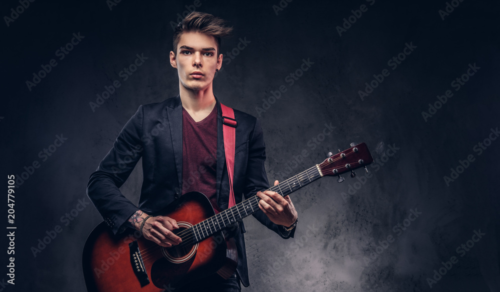 Obraz premium Stylish young musician with stylish hair in elegant clothes, playing on an acoustic guitar.