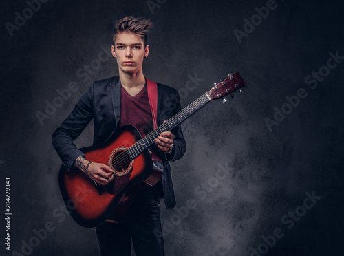 Stylish young musician with stylish hair in elegant clothes, playing on an acoustic guitar.