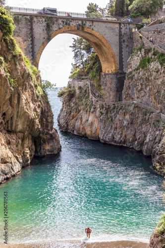 Fiordo di Furore beach. Furore Fjord, Amalfi Coast, Positano, Naples, Italy. - Men walking out the turquoise water of the beach. The bridge over the fjord and the beach.