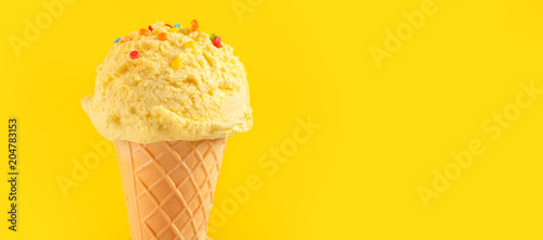 Ice cream. Vanilla, banana or lemon flavor icecream in waffle cone over yellow background. Sweet dessert decorated with colorful sprinkles closeup