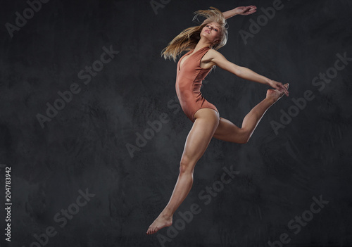Fototapeta Naklejka Na Ścianę i Meble -  Young graceful ballerina dances and jumps in a studio. Isolated on a dark background.