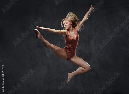 Young graceful ballerina dances and jumps in a studio. Isolated on a dark background.