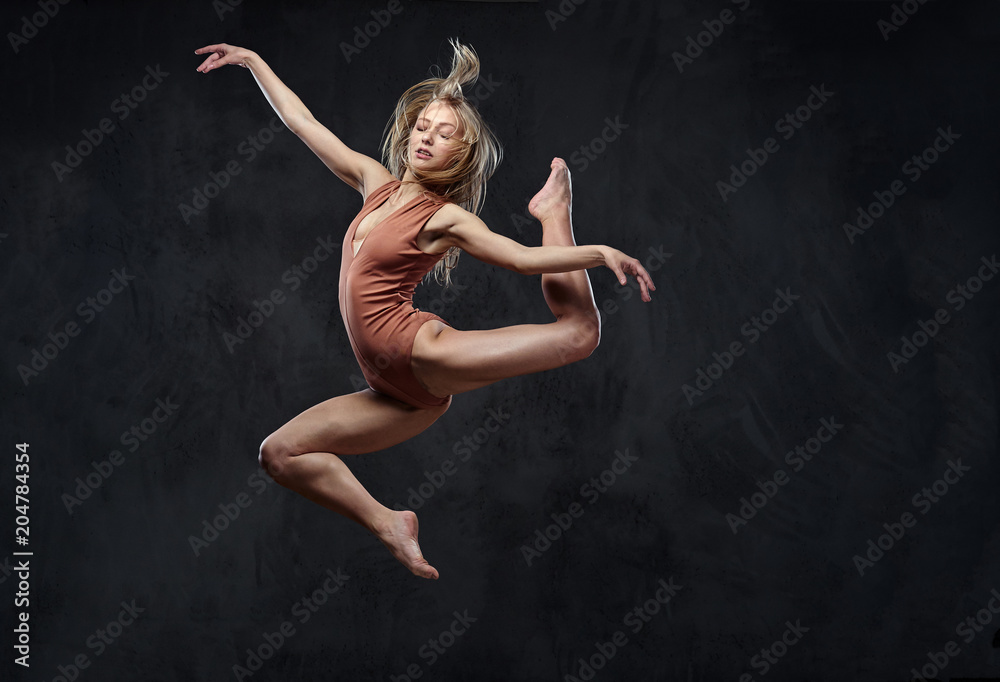 Young graceful ballerina dances and jumps in a studio. Isolated on a dark background.