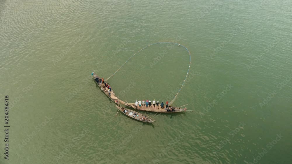 Upper view on fishers in small boats lifting together a large net out of water Upper view on fishers in small boats lifting together a large net out of water