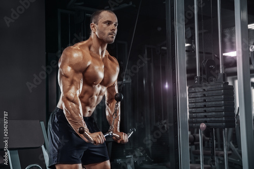 Handsome power athletic man on diet training pumping up muscles with dumbbell and barbell. Strong bodybuilder with six pack, perfect abs, shoulders, biceps, triceps and chest