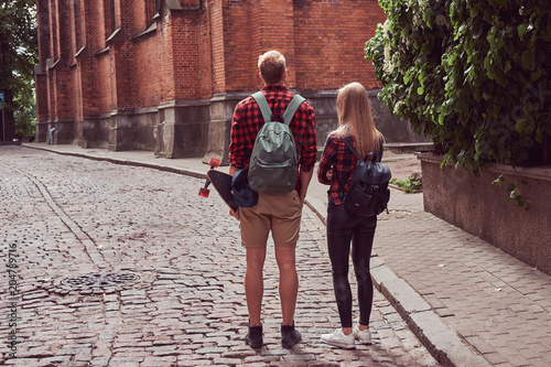 Young hipster couple, handsome skater and his girlfriend walking around an old streets of Europe.