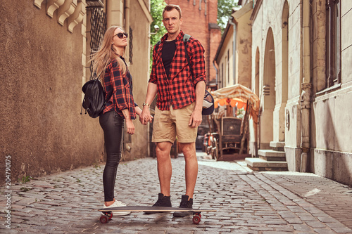 Young hipster couple, handsome skater and his girlfriend standing on old narrow streets of Europe.