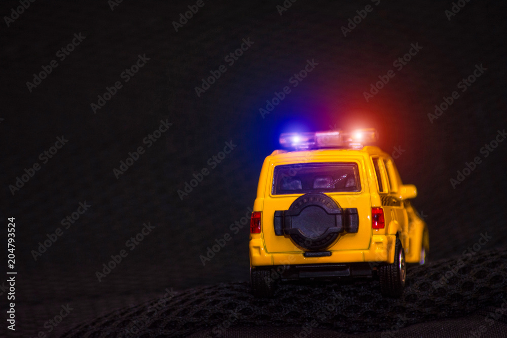 Yellow car with red and blue flashers on a black background. Children's toy car. Blurred background. Space for text. Police. Security.