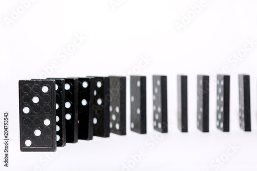 Curved row of black wooden dominoes standing on a white background. Logical Game. Business concept. Space for text.