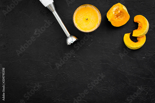 Cook orange cream soup with vegetables. Pumpkin and blender on black background top view copy space
