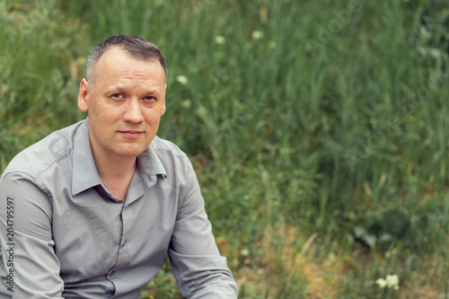 A man sitting on a grass-covered lawn and smiling or sad, looks anxiously