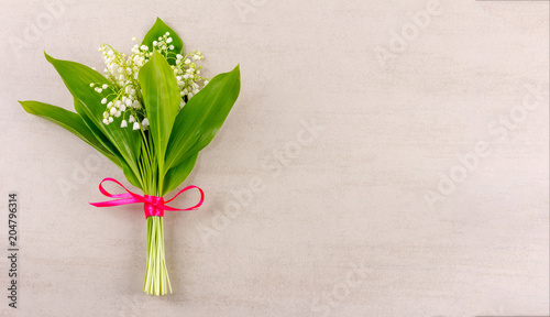 bouquet of lily of the valley flowers tied with a red ribbon on a gray wooden background with copy space