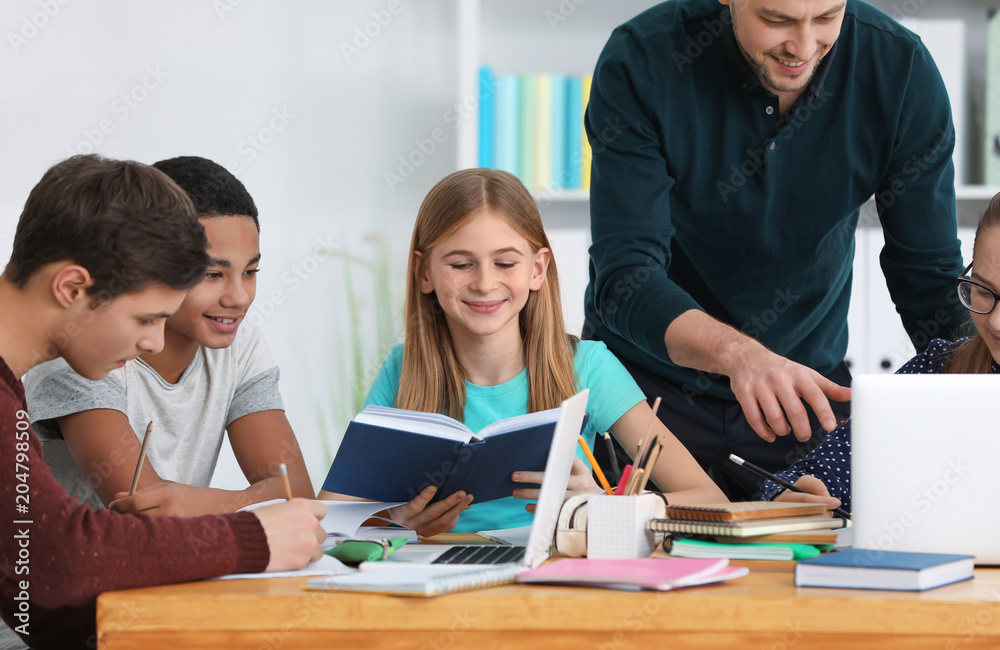 Group of teenagers doing homework with teacher in classroom Group of teenagers doing homework with teacher in classroom