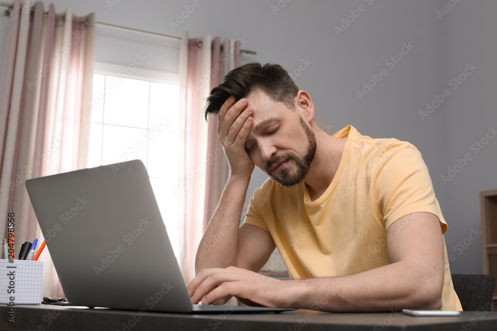 Young man working with laptop at desk in home office Young man working with laptop at desk in home office